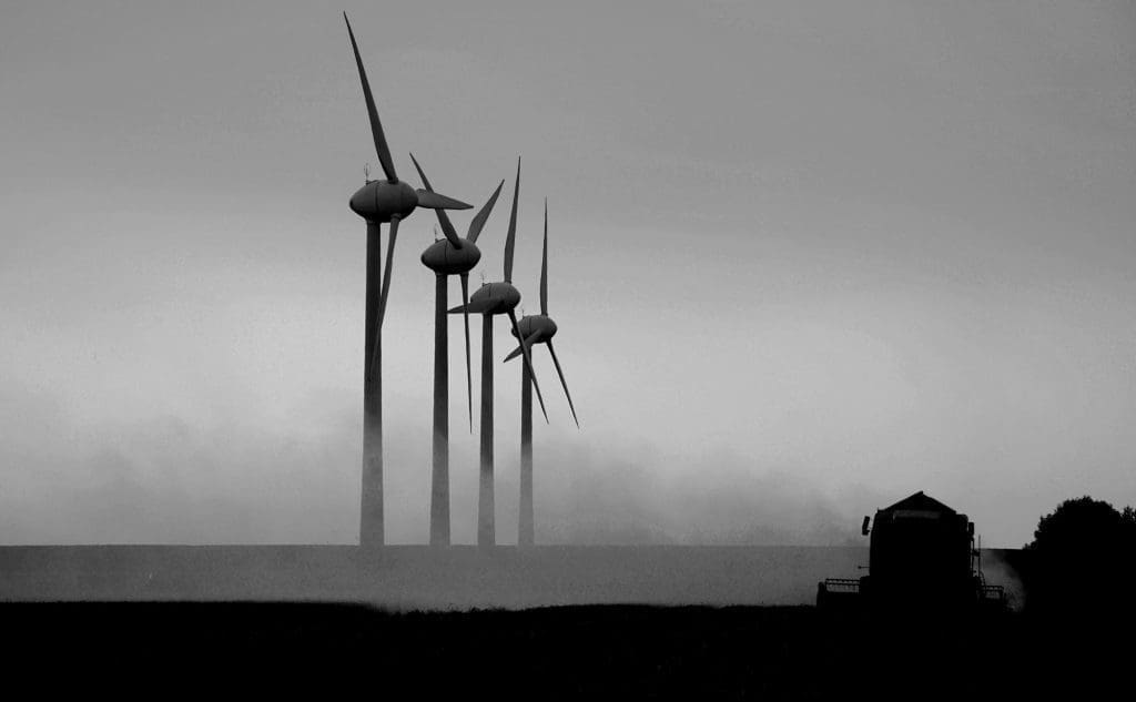 Silhouettes of wind turbines and a harvester in a field at dusk