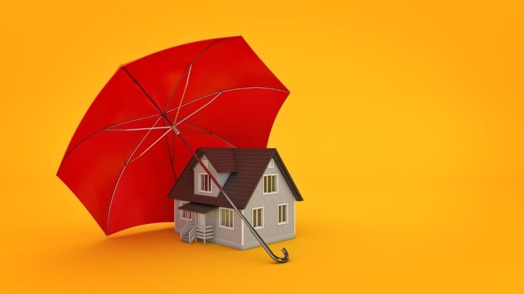 A small model of a house is positioned under a large, open red umbrella, against a solid orange background.