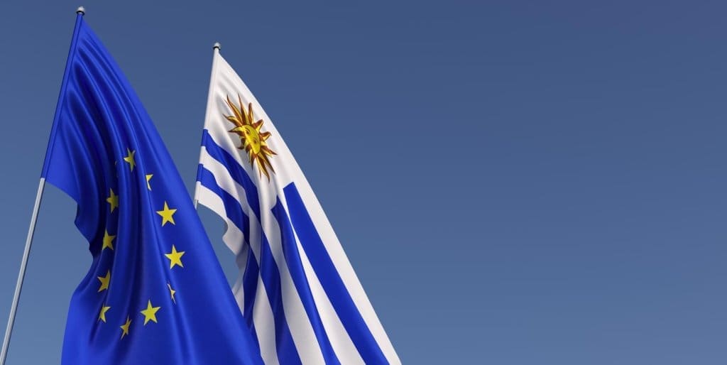 Die Flaggen der Europäischen Union und Uruguays wehen gemeinsam vor einem klaren blauen Himmel und repräsentieren die internationale Partnerschaft.