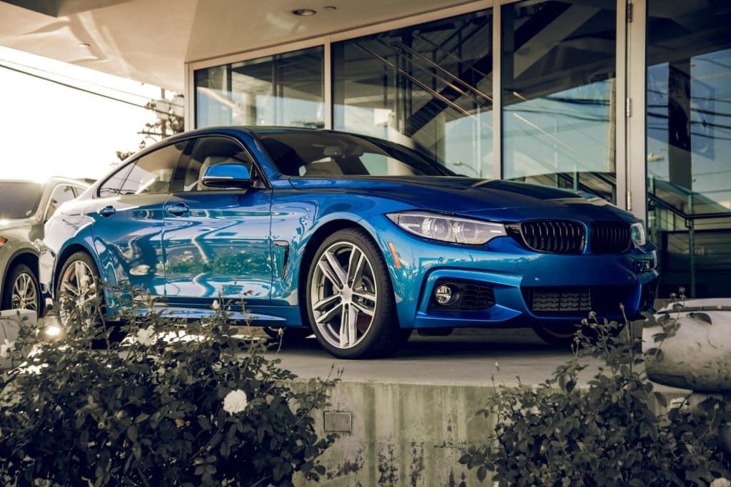 Low angle shot of a vibrant blue BMW 4 Series parked near modern glass building entrance.